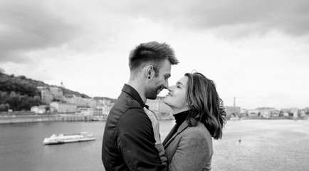 beautiful amazing sweet cheerful young couple (man and woman) standing on bridge by the river on cityscape background. Family, tenderness, dating, urban, love and friendship concept