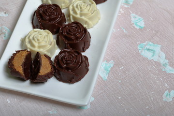 Chocolate coated sweets with almond filling. In the form of a flower. Lie on a white plate. One candy is cut to show the filling.  On an aged surface with peeling paint.