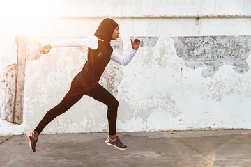 Serious muslim sports fitness woman dressed in hijab and dark clothes running outdoors.
