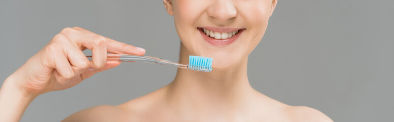 panoramic shot of happy naked woman holding toothbrush near teeth isolated on grey