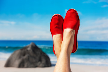Beine mit roten Stoffschuhen vor Strand und Meer