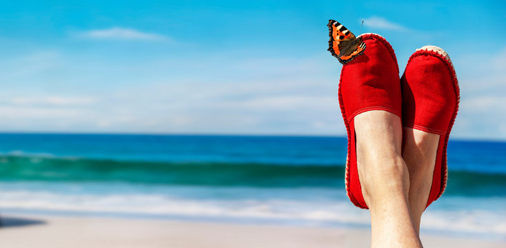 Beine mit roten Stoffschuhen vor Strand und Meer