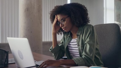 Stressful young businesswoman at desk using laptop - Powered by Adobe