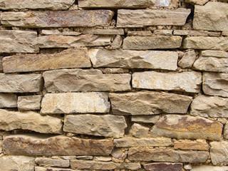 Fragment of masonry made of yellow and brown stone under natural light, close-up