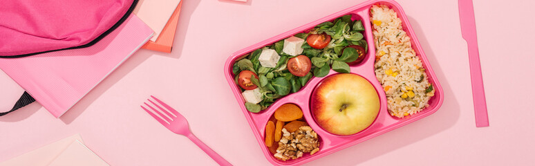 panoramic shot of lunch box with food near fork, backpack and stationery