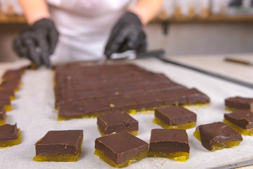 Divide fillings for chocolate candies praline with apricot marmalade using spatula. Baker's hands on background