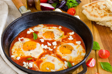 Shakshouka, dish of eggs poached in a sauce of tomatoes, chili, onions in the pan.