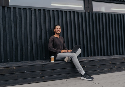 Freelancer Man siting in urban city with a laptop phone camera and coffee or tea with misic headphones