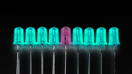 Stand out from the crowd and be different concept: one purple LED between eight cyan ones. Black...