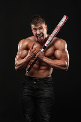 Brutal strong muscular bodybuilder athletic man pumping up muscles with baseball bat on black background.