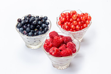 Blueberries, raspberries, currants in glass plates on a white background. Isolated
