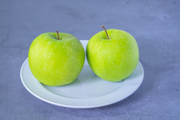 Fresh green apples in White ceramic plate, on On the cement floor.