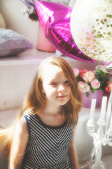 Girl is sitting in a room with balloons and smiles