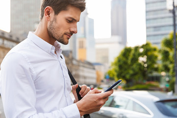 Young businessman walking by street using mobile phone chatting.