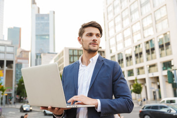 Fototapeta premium Serious handsome young business man standing near business center using laptop computer.