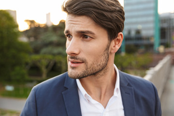Serious concentrated unshaved businessman outdoors on the street looking aside.