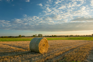 Hay bale on stubble during sunset and clouds in the sky