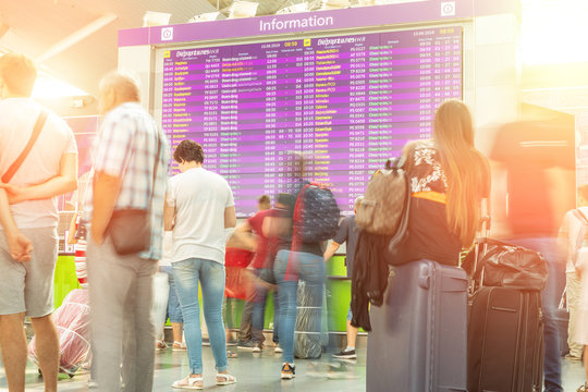 Motion Blurred Travellers Crowd Looking At Fligh Feparture And Arrival Timetable At Airport Terminal. Travel And Tourism Concept. Flight Delay