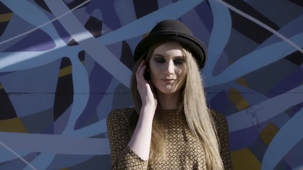 Portrait of young beautiful fashionable woman with black hat posing on blue graffity background. Action. Model wearing stylish wide-brimmed hat looking at camera, female fashion.