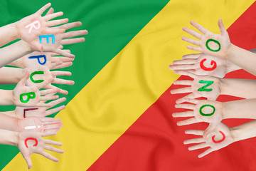 Inscription Republic of the Congo on the children's hands against the background of a waving flag of the Republic of the Congo