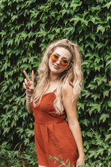 A beautiful woman in her twenties wearing 70s style clothing and sunglasses posing for portraits and smiling 