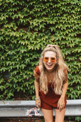 A beautiful woman in her twenties wearing 70s style clothing and sunglasses posing for portraits and smiling 