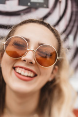 A beautiful woman in her twenties wearing 70s style clothing and sunglasses posing for portraits and smiling 