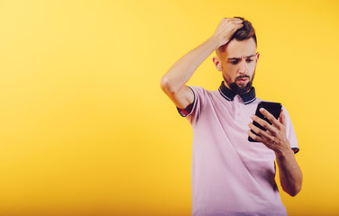 Stylish male in bright T-shirt browsing mobile phone while standing against bright yellow background. Place the text, coppy paste.