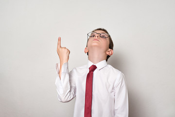 Boy in a white shirt and glasses points his finger up. School concept. White background.
