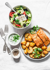 Mediterranean lunch table - baked lemon salmon with potatoes, greek salad, tzadziki sauce on light background, top view. Flat lay