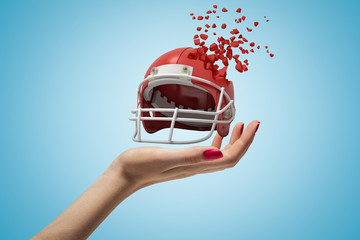 Closeup of woman's hand holding sports helmet which is breaking into small pieces that are flying...