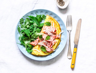 Omelet with green salad and baked salmon on a light background, top view. Healthy breakfast, snack