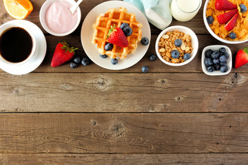 Breakfast food top border. Fruits, cereal, waffles, yogurt and coffee. Top view over a dark wood background with copy space.