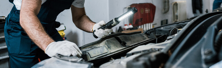 panoramic shot of auto mechanic holding flashlight near car - obrazy, fototapety, plakaty