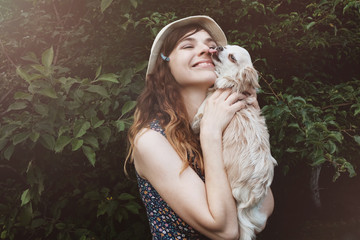 Happy caucasian young woman  in straw hat embracing pet and having fun with her dog. Little cute dog licking it's owner. 