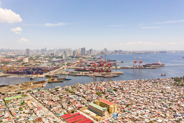 Obraz premium Port in Manila, Philippines. Sea port with cargo cranes. Cityscape with poor areas and business center in the distance, view from above. Asian metropolis.