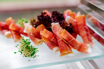 Prosciutto rolls with cream cheese decorated with lettuce and chili pepper. Snacks at the wedding reception