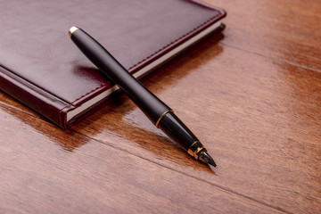 Pen and leather diary on a wooden table