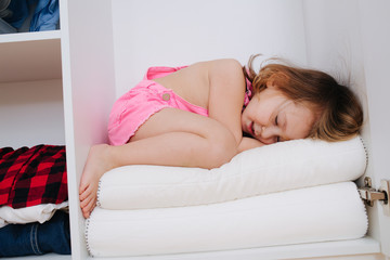 Naklejka premium Portrait of little girl in new pink overalls playing inside of open wardrobe