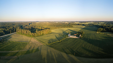Aerial view over rural landscape in a warm summer sunset tones. Agriculture land mixing with forest and meadows. Green crop fields along the curved river. Trees creating long shadows. 