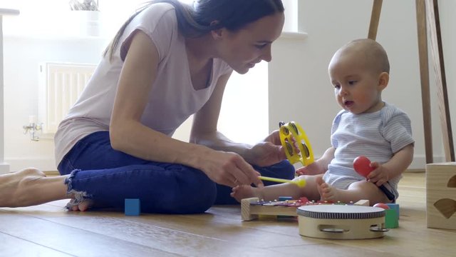 Mother With 8 Month Old Baby Boy Playing With Musical Instruments At Home   