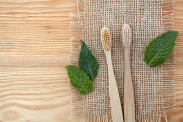 Zero waste concept. Bamboo toothbrush on wooden background with green mint leaf. Plastic free essentials, teeth care.