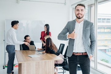 Portrait of happy businessman standing in modern meeting room.Casual business man with arms crossed.Young businessman thumbs up posing and smiling at camera.