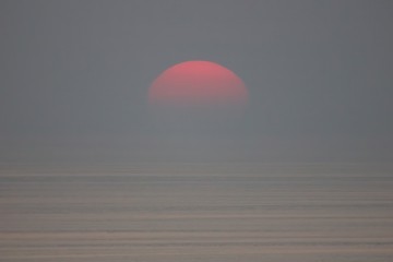 The sun is falling into the sea and being partially swallowed by the fog.  sky  is dark