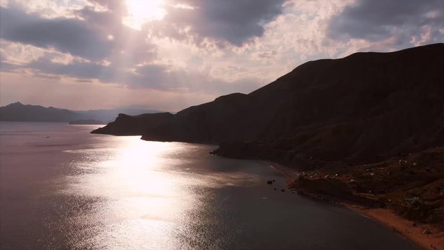 Beautiful panoramic view of the mountains and the sea, filming from above. Aerial shooting from the shoreline on an overcast day, the sun's rays make their way through the clouds, beautiful light