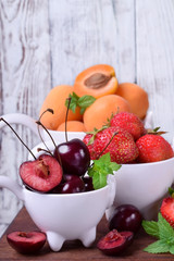 Cherries, strawberries and apricots in little white cups on the wooden table