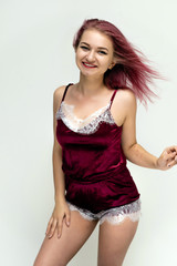 Fototapeta premium Concept portrait of a knee-high pretty sexy girl with purple hair in beautiful red lingerie on a white background. She smiles, happy with life, happy. Hair flying, front view. Made in a studio.