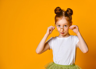 Beautiful young girl with red hair with a bagel in her stylish glasses looks at you in the frame.