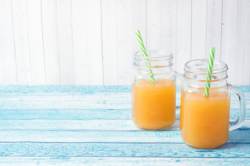Orange juice in glass jars and fresh oranges on a blue background.