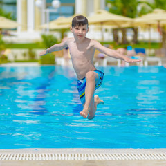 Naklejka premium Caucasian boy having fun making fantastic jump into swimming pool at resort. He is enjoying his summer vacations.